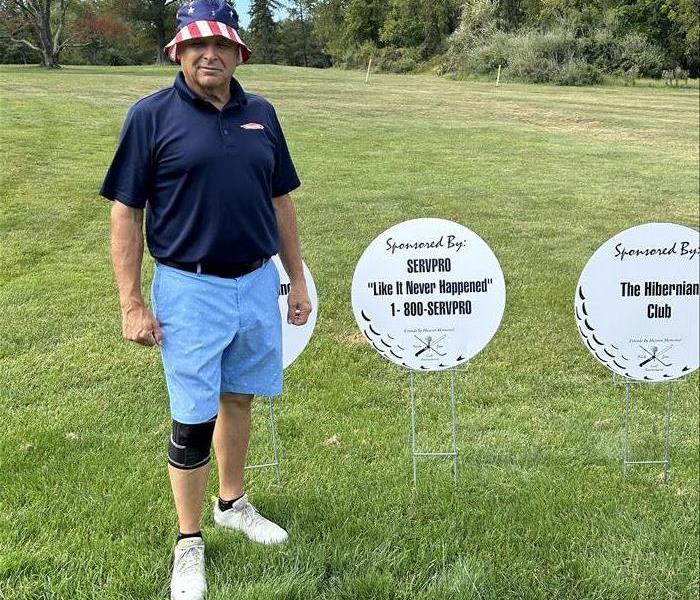 man standing next to golf sponsor sign